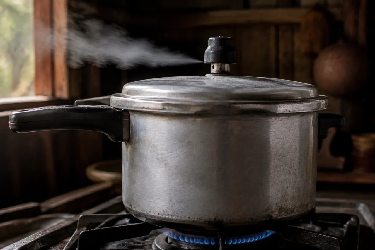 Panela de pressão fechada sobre a boca do fogão, com um fio de vapor saindo da válvula e a chama baixa e azul embaixo.